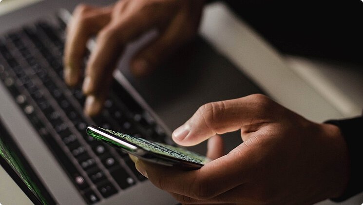 [Translate to German:] person typing on laptop holding phone